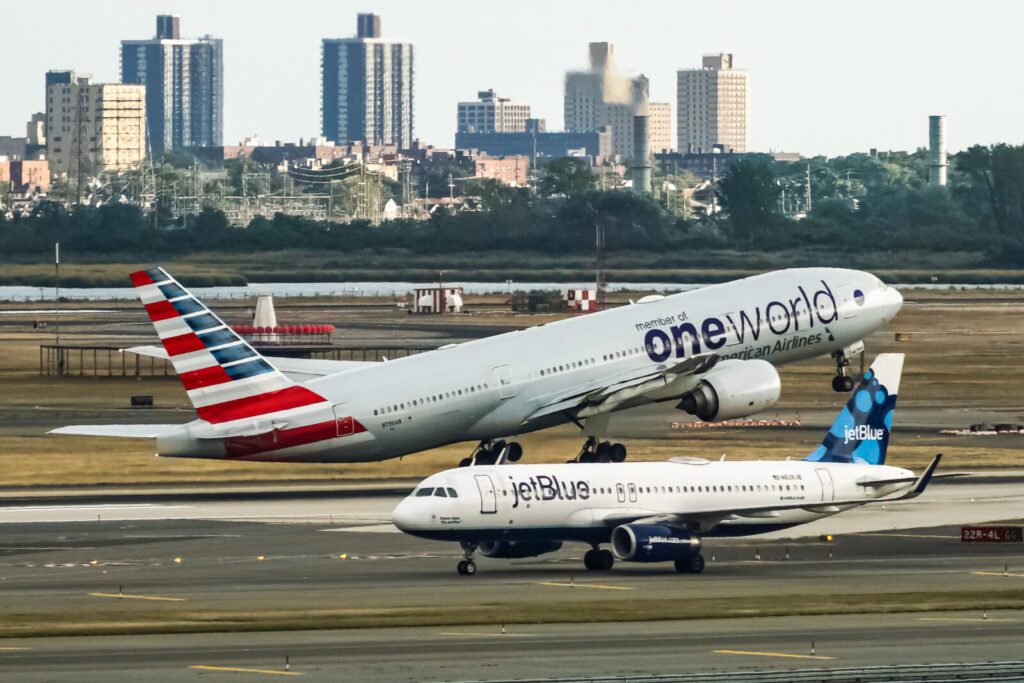an american airlines plane taking off with a jetblue plane taxiing in the foreground