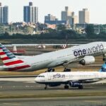 an american airlines plane taking off with a jetblue plane taxiing in the foreground