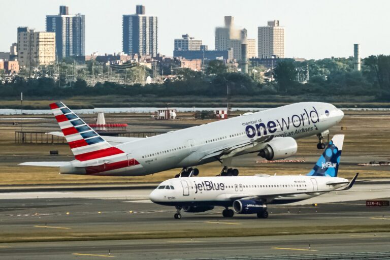 an american airlines plane taking off with a jetblue plane taxiing in the foreground
